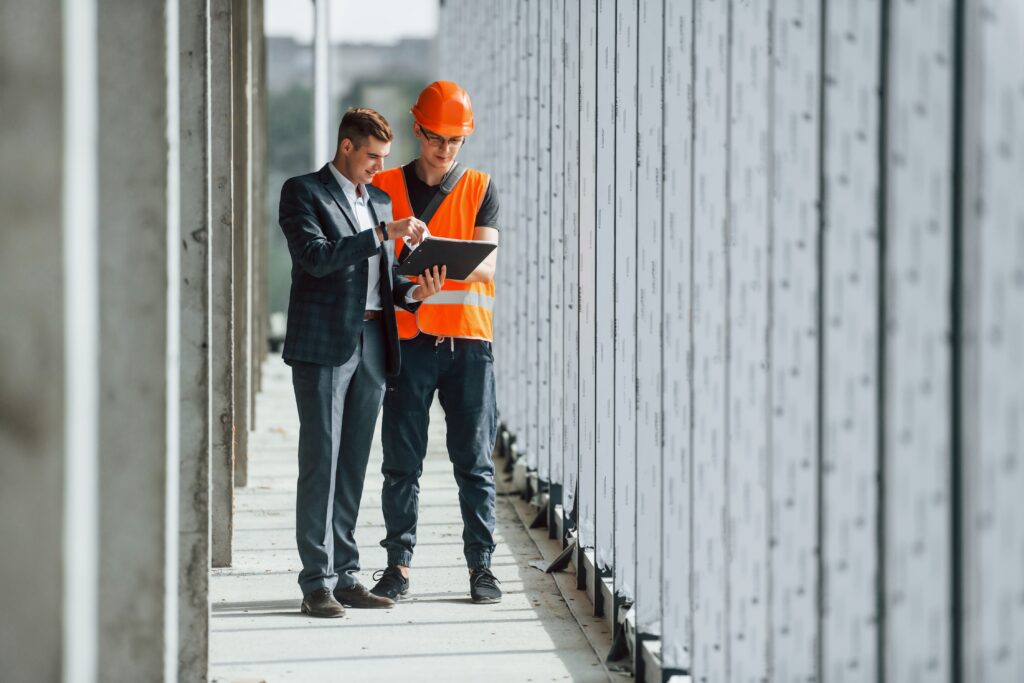 Two men reviewing construction industry accounting documents on a tablet at a construction site