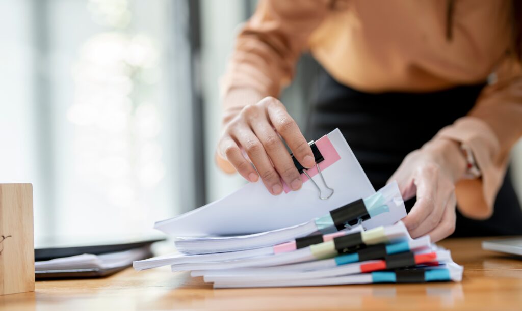 A female accountant reviewing stacks of paper files for a public accounting audit