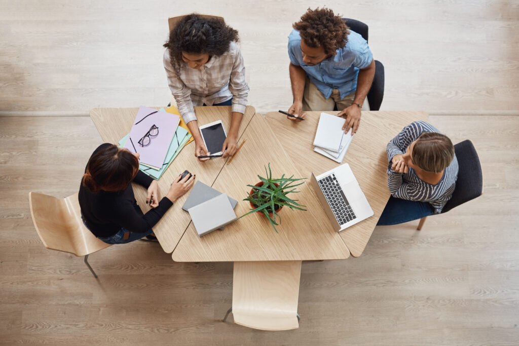 A team of broker dealers sitting at a table discussing an RIA audit with laptops and smartphones