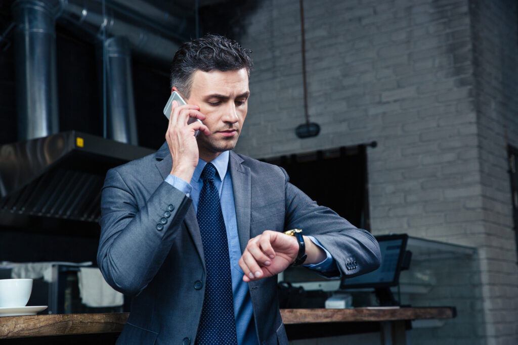 A confident business man on the phone looking at his watch realizing the company's yearly audit is coming up