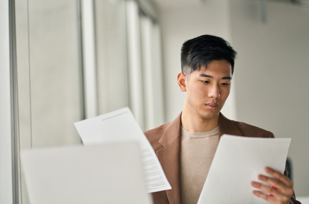 A young asian businessman reading legal documents to for the upcoming statutory audit of his nonprofit