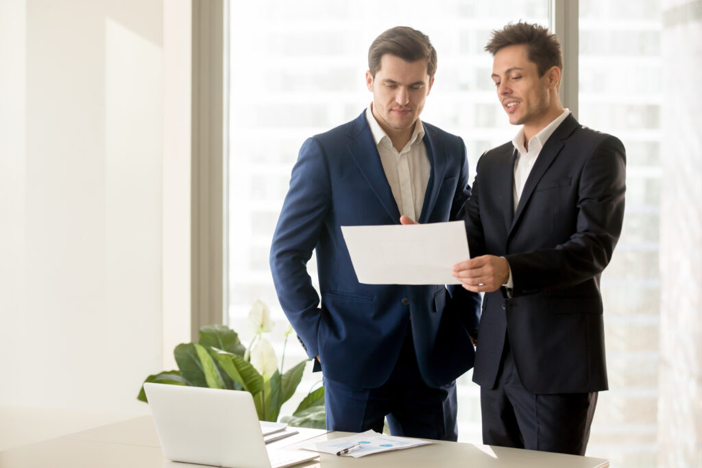 Two smiling businessmen reviewing a document in an office, discussing GAAP audited financial statements.