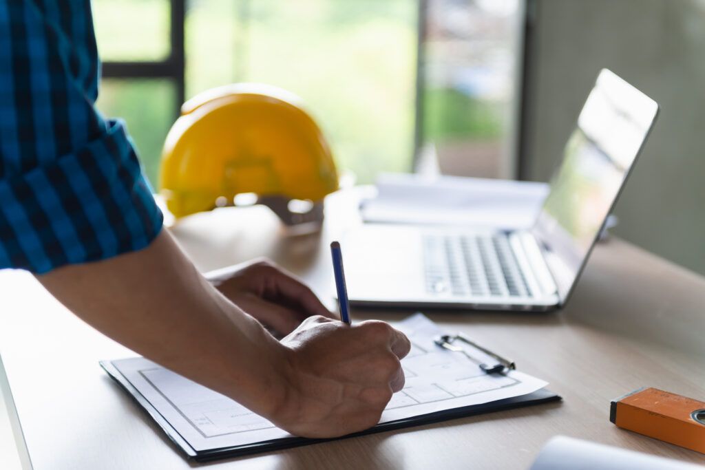 Person updating documents at a desk with a laptop and hard hat, illustrating WIP construction accounting practices.