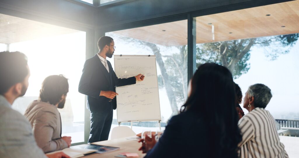 Presenter leads a meeting beside a flip chart while a team listens during a private equity audits discussion.
