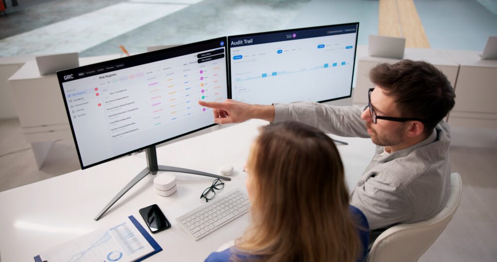 Independent auditors report preparation as two professionals review risk and audit trail dashboards.