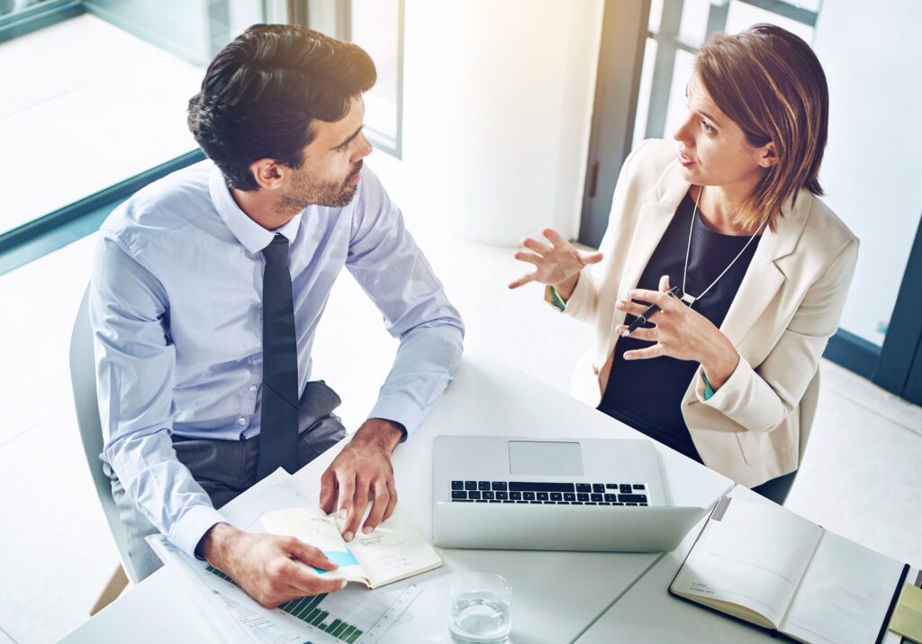 Two professionals discuss documents beside a laptop while reviewing an independent auditors report.