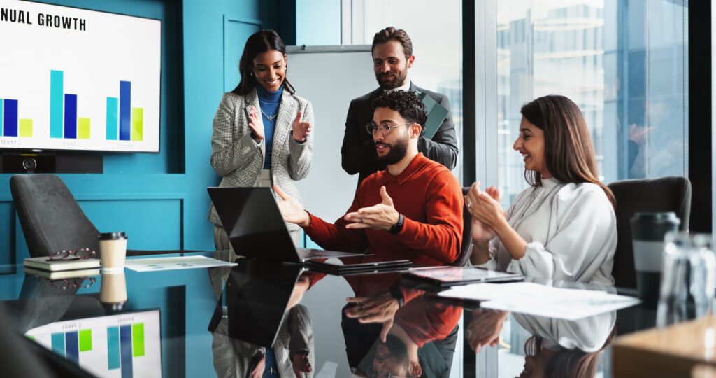 Federal grant audits discussed by a business team applauding around a laptop in an office.